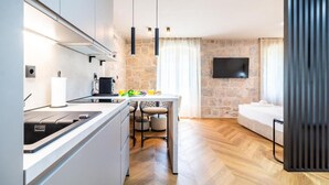 A modern kitchen with a dining area, a sofa, and a TV mounted on the wall. - Apartments Centre In Stone House (Split)
