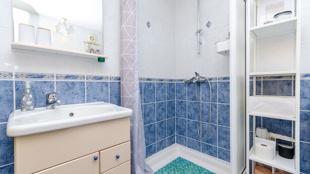 Un baño con lavamanos, ducha y repisas con artículos de tocador.