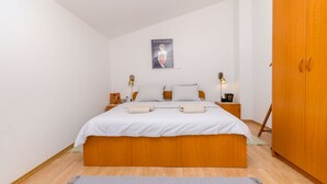 A bedroom with a large bed, wooden wardrobe, and a poster on the wall. - Apartment Marisa (Hvar)