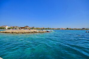 Una zona costiera con acque cristalline blu, una spiaggia sabbiosa e diversi edifici sullo sfondo.
