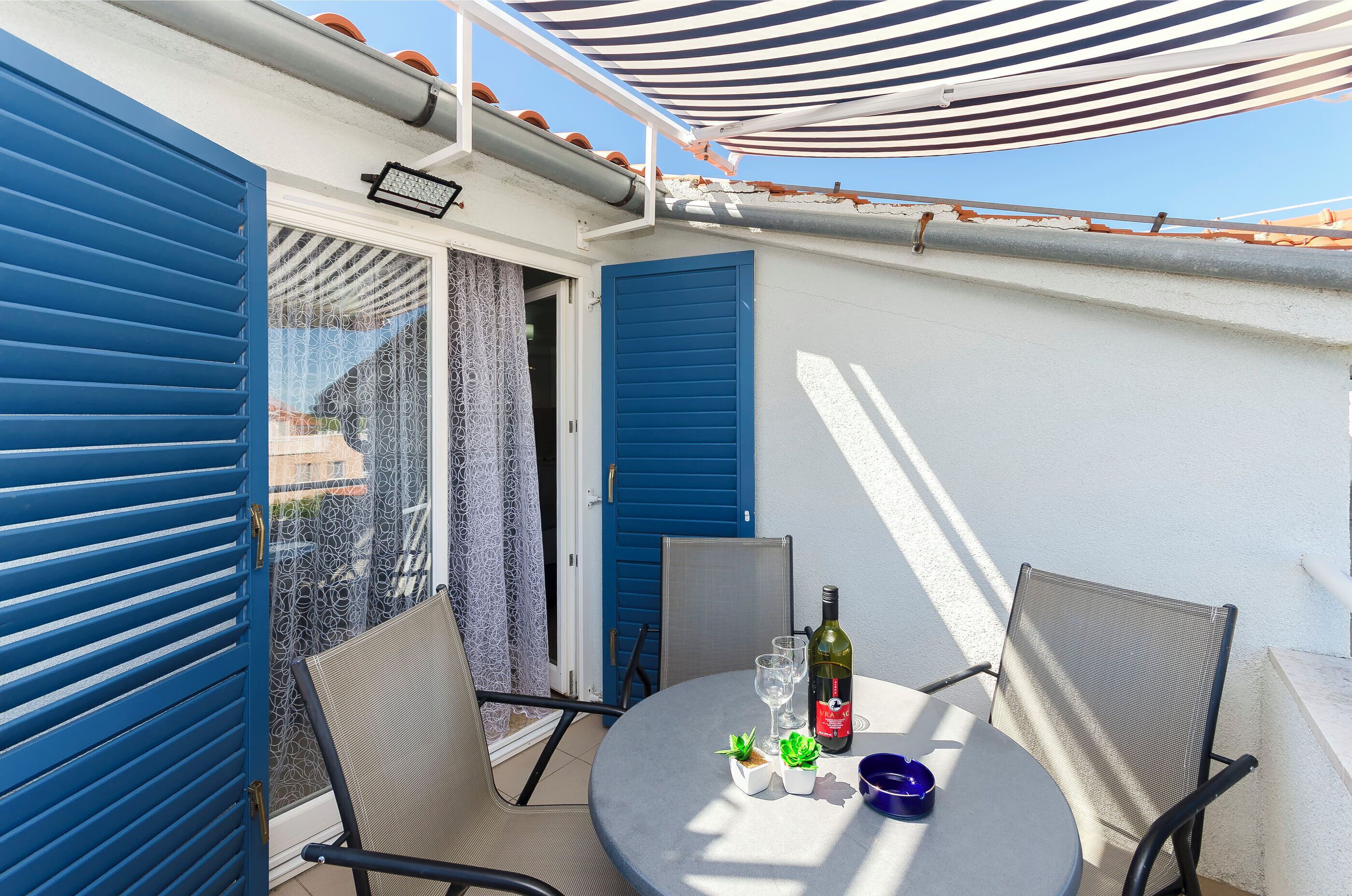 Ein Balkon mit Tisch, Stühlen, einer Flasche, Gläsern und kleinen Pflanzen.