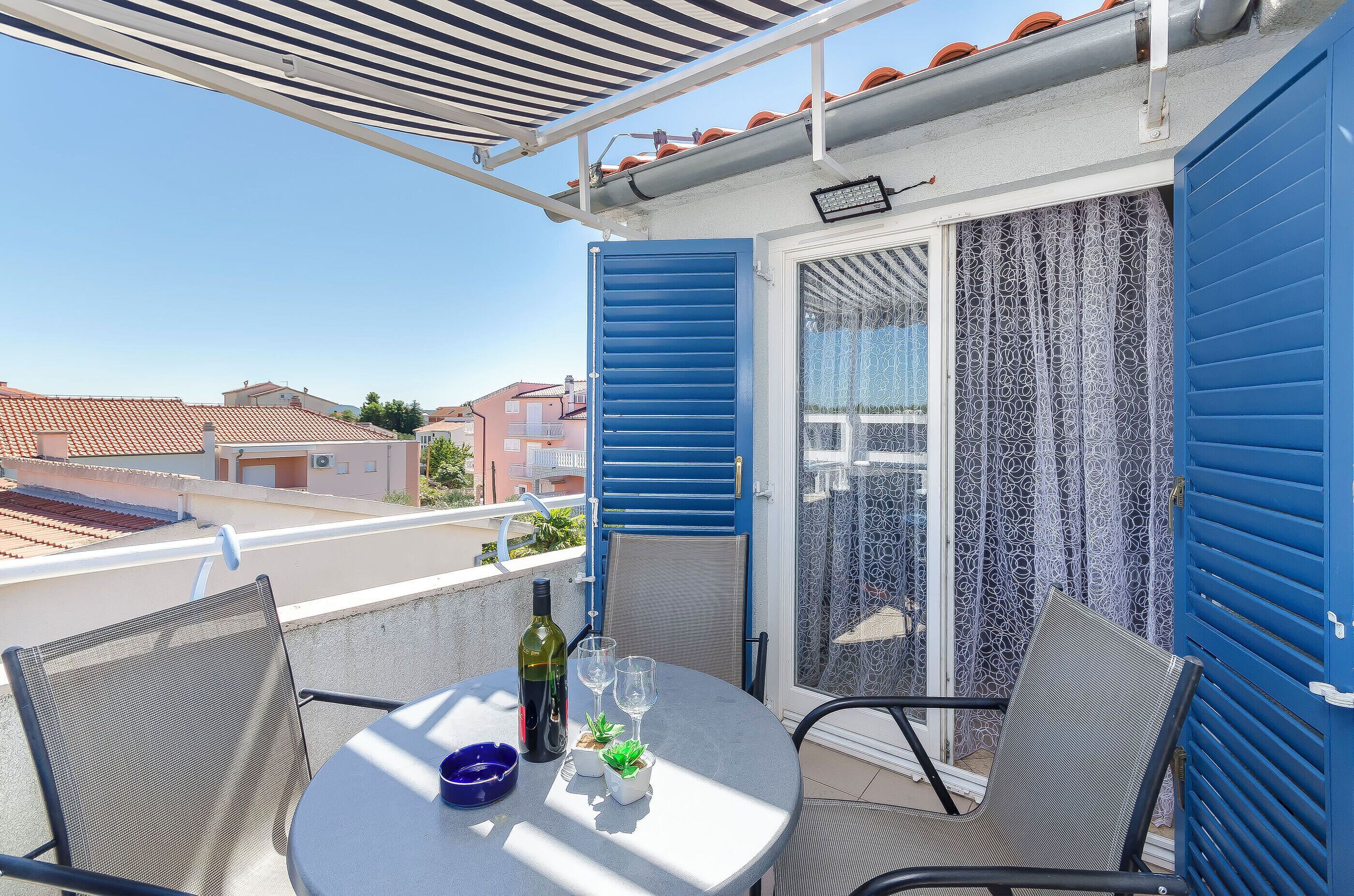 A balcony with a table, chairs, a bottle, and glasses.