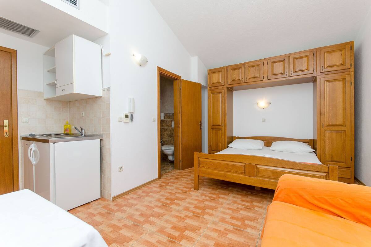 Een kleine kamer met een bed, een kitchenette en een badkamer.