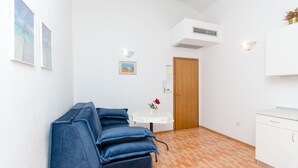 Una habitació amb un sofà blau, una taula rodona petita amb un ram i una porta de fusta.
