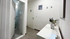 A hallway with a glass door leading to a bathroom, a white door, and a white counter with a plant. - Apartments Apartments -T and T (Okrug)