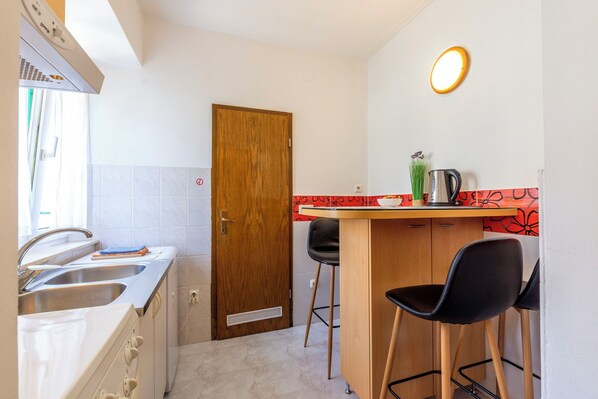 A compact kitchen with a wooden door, a sink, and a small bar area with stools. - Apartment Center With Jacuzzi (Split)