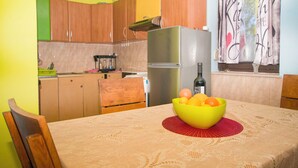 A kitchen with wooden cabinets, a stainless steel refrigerator, and a table with a yellow bowl of fruit. - House Cross (Zemunik Donji)