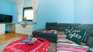 A living room with a sofa, a TV, a window with curtains, and a small table with a bowl and remote. - House Cross (Zemunik Donji)