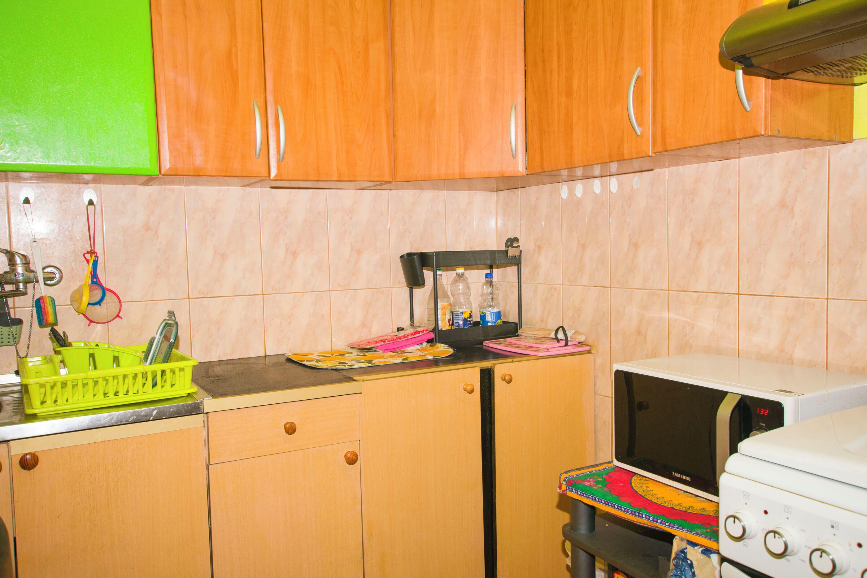Une cuisine avec des meubles de rangement en bois, un four à micro-ondes, une cuisinière et un égouttoir à vaisselle vert.