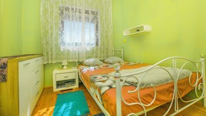 A bedroom with a bed, a nightstand, a dresser, and a window with lace curtains. - House Cross (Zemunik Donji)