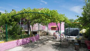 A courtyard with a pergola covered in green vines, a pink wall, and a red bench. - House Cross (Zemunik Donji)