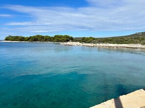 A coastal scene with clear turquoise water, a sandy beach, and a rocky outcrop with trees. - House Sunshine (Pasman)
