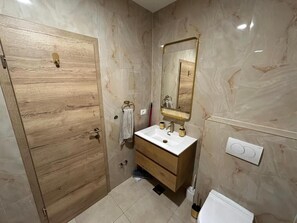A bathroom with a wooden door, a white sink, a mirror, and a toilet. - House Sunshine (Pasman)