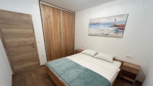 A bedroom with a wooden bed, a nightstand, a wooden wardrobe, and a painting on the wall. - House Sunshine (Pasman)