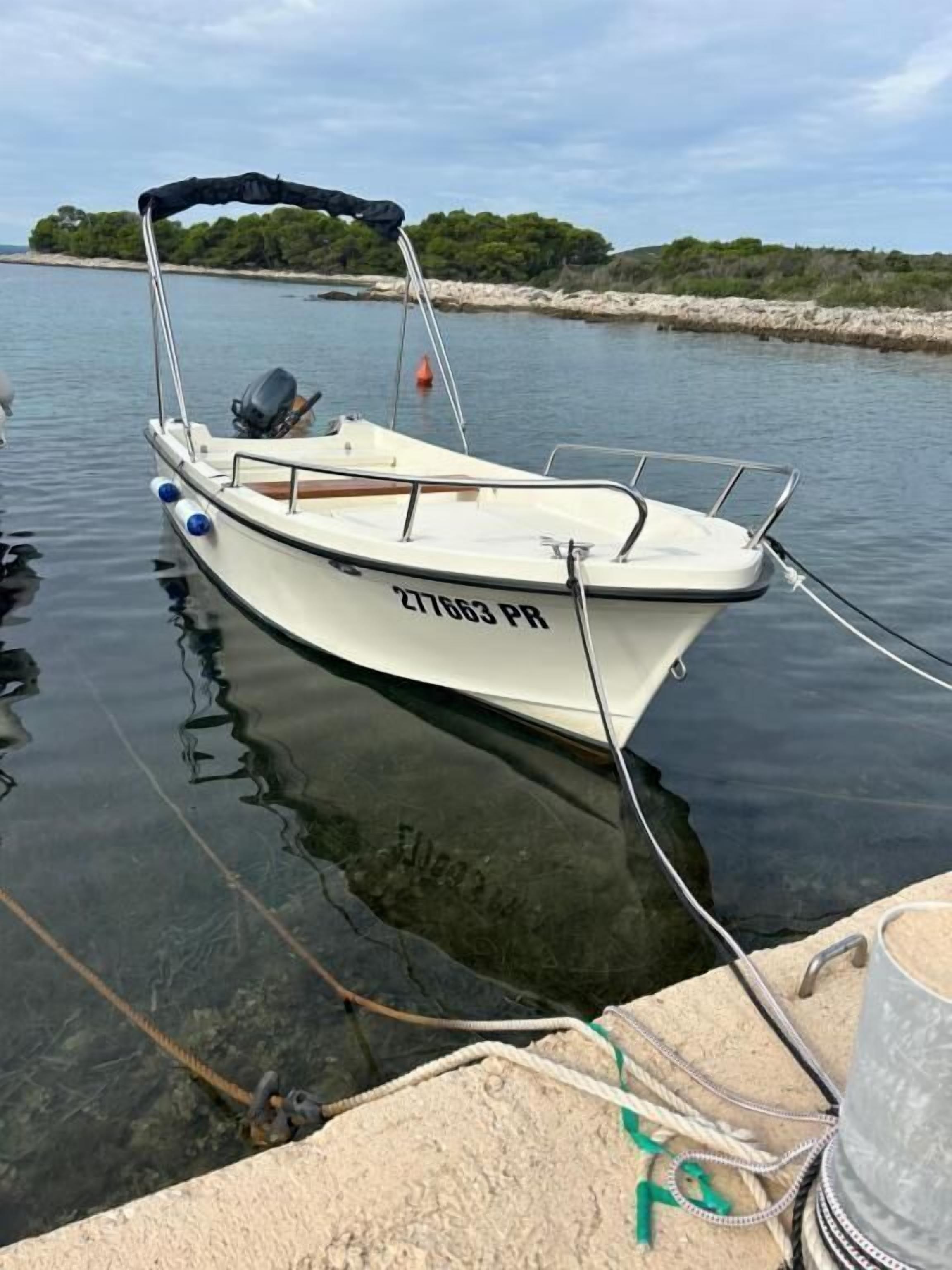 A small white boat with the registration number 217663 PR docked at a pier.