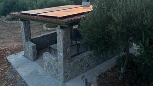 A stone-built outdoor structure with a roof, surrounded by vegetation and overlooking a body of water. - House Sunshine (Pasman)