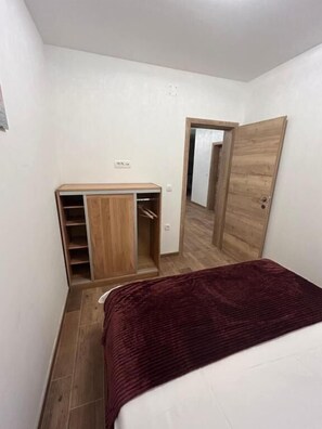 A small, narrow room with a wooden wardrobe, a mirror, and a bed with a red blanket. - House Sunshine (Pasman)
