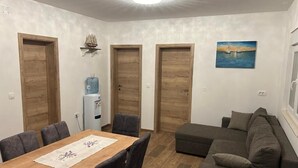A room with a wooden dining table, grey chairs, a grey sofa, and a water dispenser. - House Sunshine (Pasman)