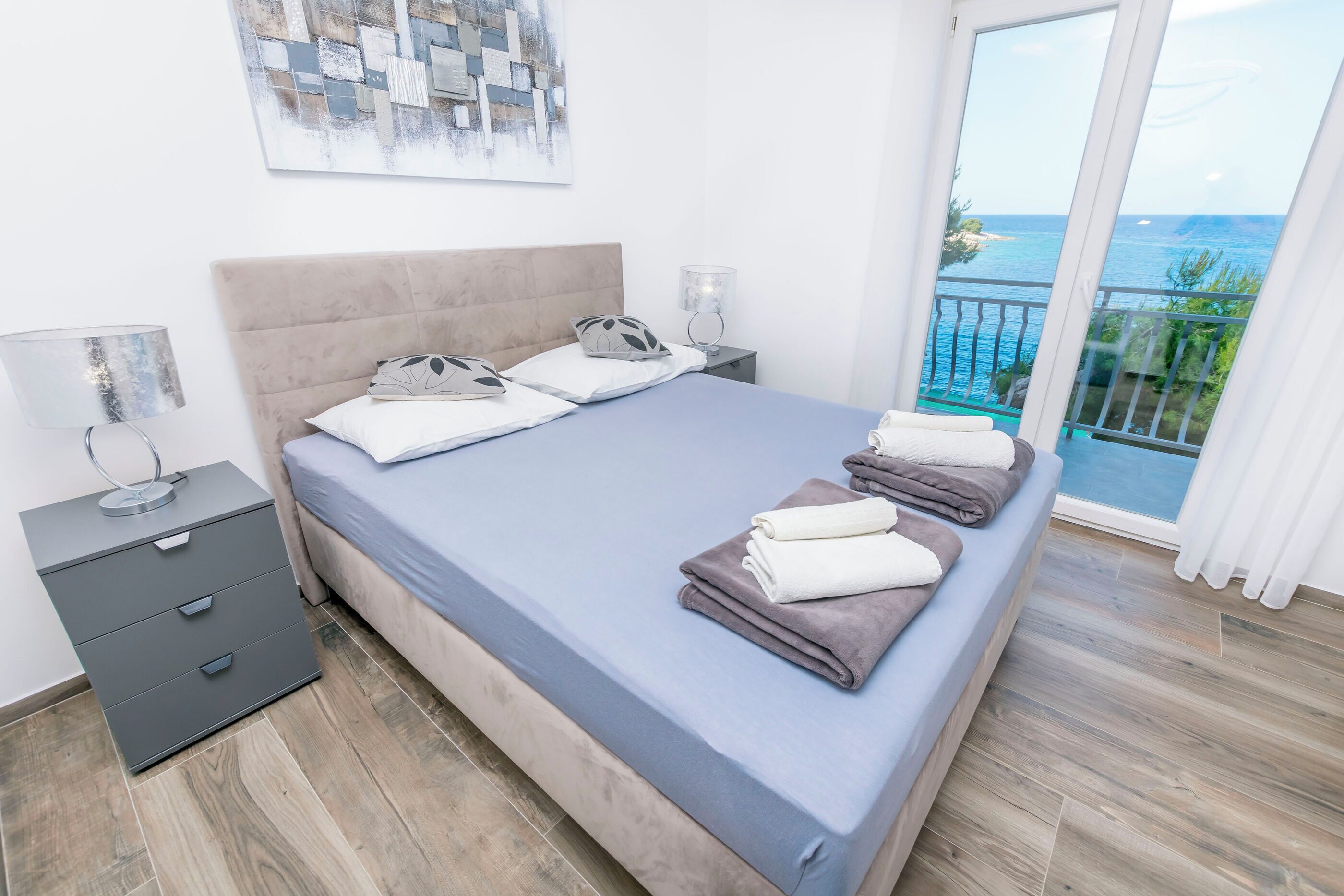 A bedroom with a bed, bedside tables, and a view of the sea.
