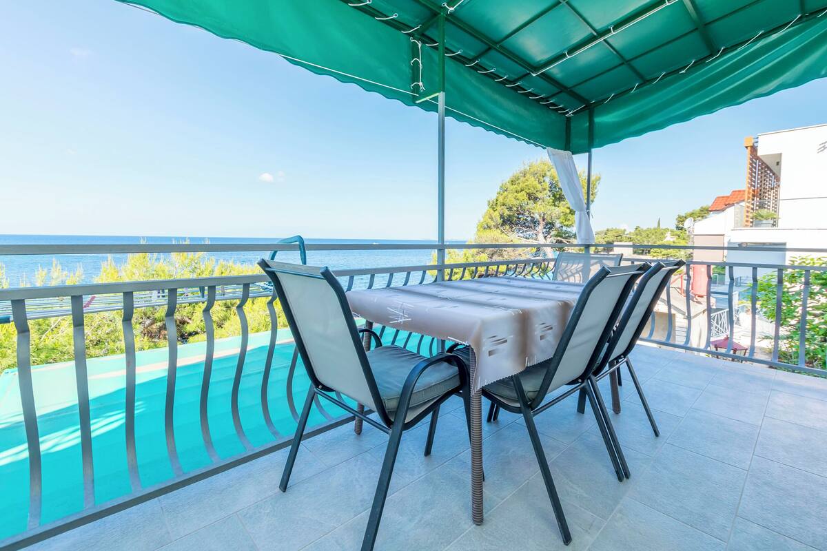 An outdoor patio with a table and chairs overlooking a swimming pool and the sea.