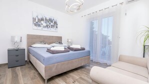 Ein modernes Schlafzimmer mit Bett, Nachttischen, einer Lampe, einer Couch und einem großen Fenster mit Blick.