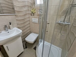 A modern bathroom with a glass-enclosed shower, a white sink, and a toilet. - Apartments Fenix (Primosten)