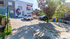 A residential street with a white car parked on the left, a black car on the right, and a tree in the center. - Apartment Simun (Rogoznica)