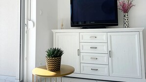 A room with a white cabinet, a flat-screen TV mounted above it, a small round table with a plant and a teapot, and a sliding glass door. - Apartment Simun (Rogoznica)