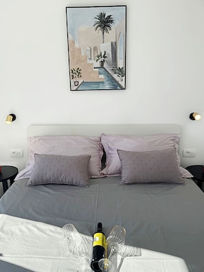 Een bed met twee kussens, een fles en twee glazen op een witte spreidek.