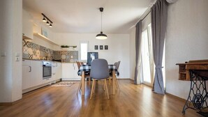 Eine moderne Küche mit weißen Schränken, einem eingebauten Backofen und einer gefliesten Spritzschutzwand. Es gibt einen Essbereich mit Tisch und Stühlen sowie ein großes Fenster mit Vorhängen.