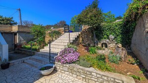 Eine steinerne Treppe führt zu einem Garten mit einer Statue, umgeben von verschiedenen Pflanzen und Blumen.