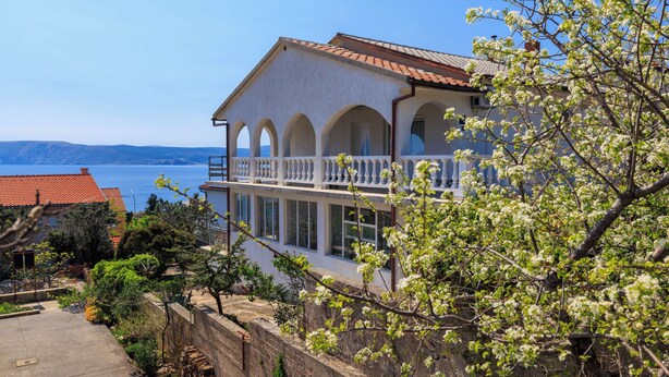 Ein zweistöckiges Gebäude mit einem Balkon, Bogenfenstern und Blick auf das Meer.