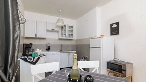 Eine kleine Küche mit weißen Schränken, einer Mikrowelle und einem Tisch mit einer Flasche und Gläsern.