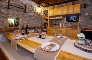 A rustic dining area with stone walls, wooden cabinets, and a long table set for four. - House Mala Kuca (Promina)