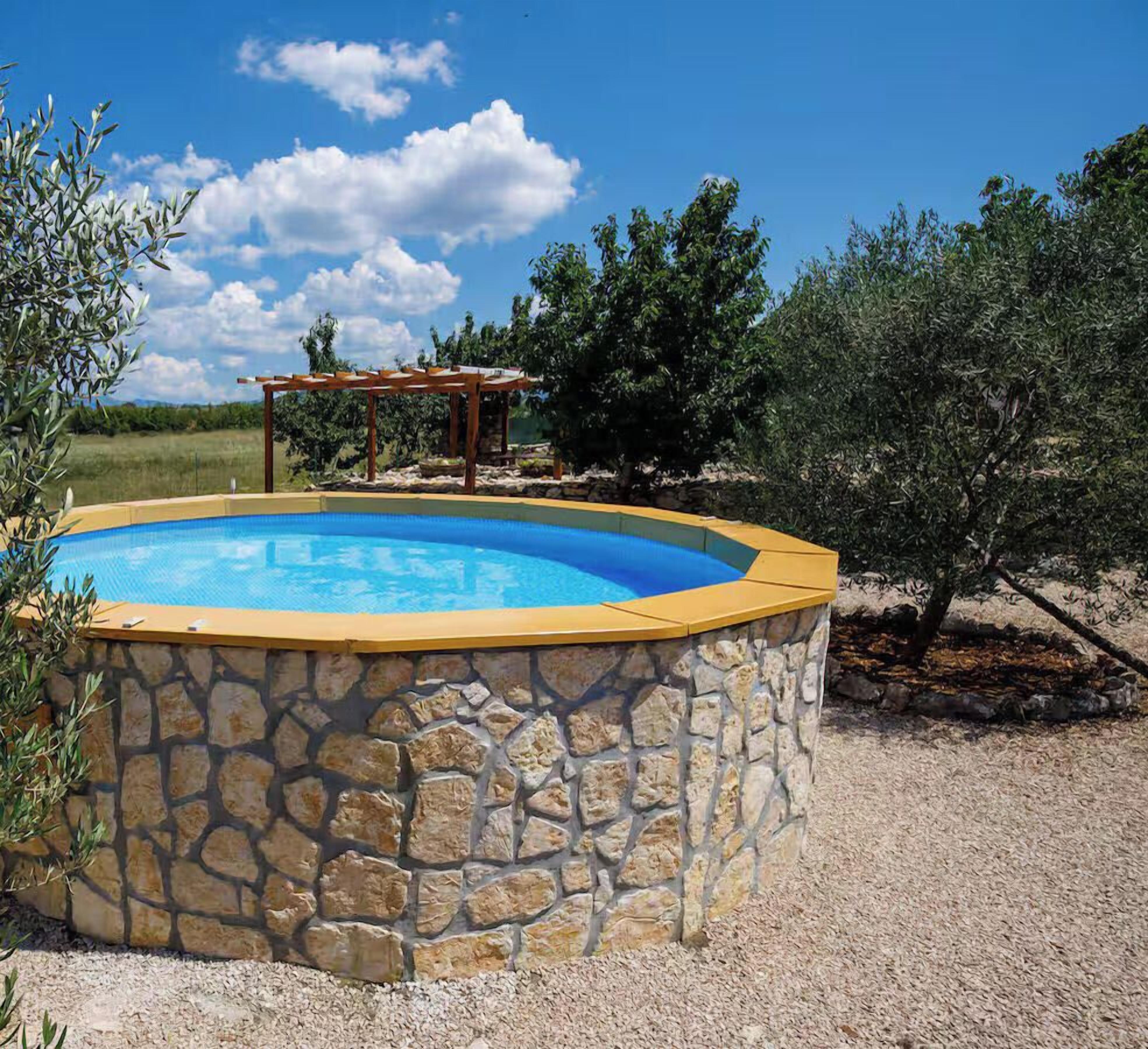 Una piscina con un muro de piedra, rodeada de grava y árboles.