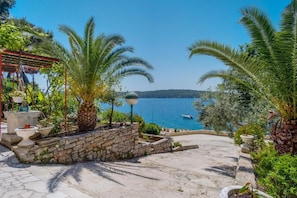 A stone pathway leading to a terrace with palm trees and a view of the sea. - Apartments Villa Magnolia (Mali Losinj)