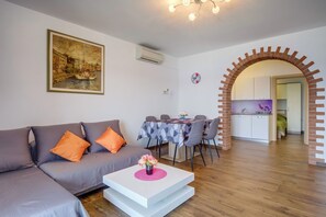 A modern living room with a grey sofa, a white coffee table with a vase, a dining area with a table and chairs, and a kitchen visible through an archway. - Apartments Villa Magnolia (Mali Losinj)