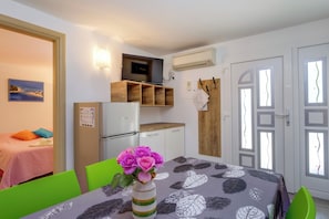 A compact room with a bed, a dining table with a vase of flowers, a refrigerator, and a wall-mounted TV. - Apartments Villa Magnolia (Mali Losinj)