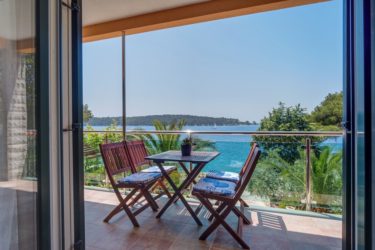 Varanda com mesa e cadeiras, oferecendo uma vista panorâmica do mar e vegetação.