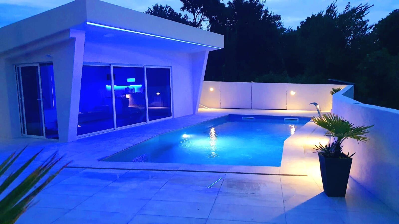 A modern outdoor pool area with a rectangular pool, a glass-enclosed lounge, and ambient lighting.