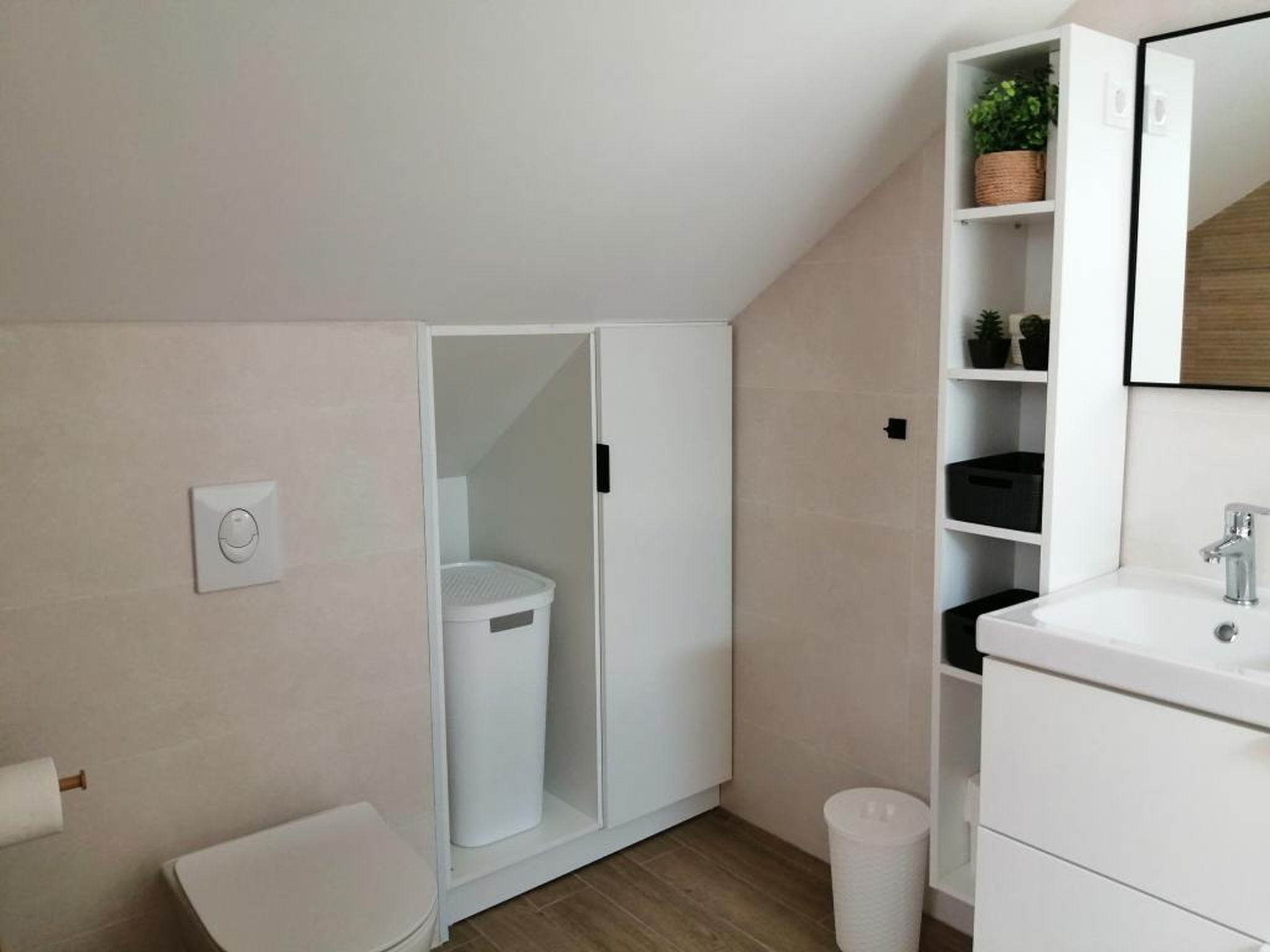 A modern bathroom with a toilet, a white sink, and a cabinet with a mirror.