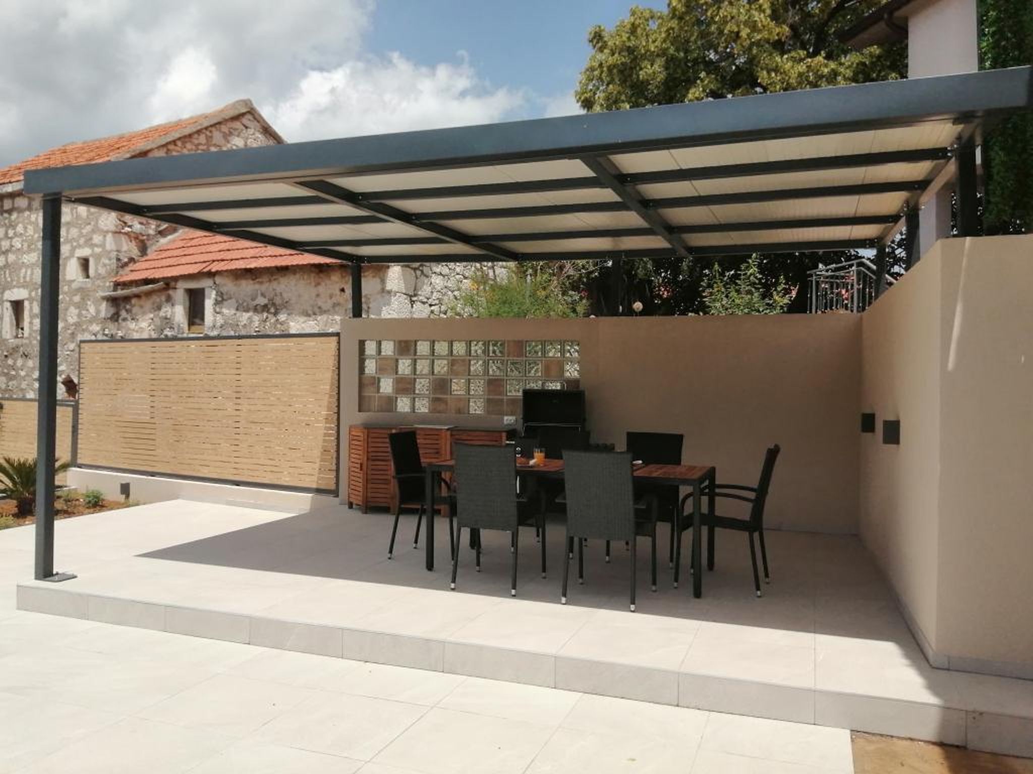 Eine überdachte Terrasse im Freien mit Tisch, Stühlen, einem Grill und einer Zierwand.