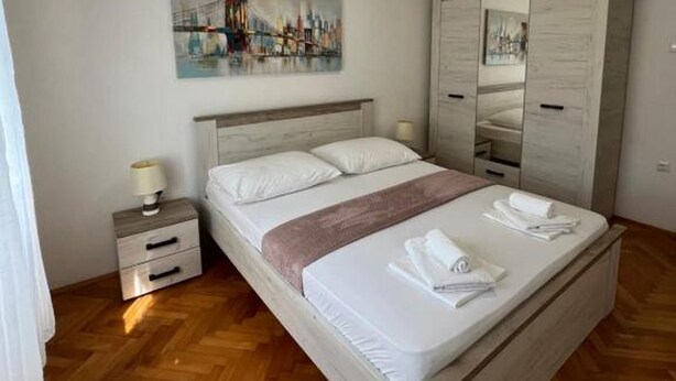 Ein Hotelzimmer mit Holzboden, einem Bett mit weißer Bettwäsche, einem Nachttisch mit Lampe, einem Gemälde an der Wand und einem Kleiderschrank.