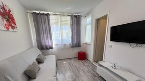 Ein modernes Wohnzimmer mit einer grauen Couch, einem flachbildfernseher an der Wand und Holzböden.