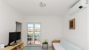 Ein Zimmer mit Bett, Schreibtisch, Computer, Fernseher und Fenster mit Blick ins Freie.