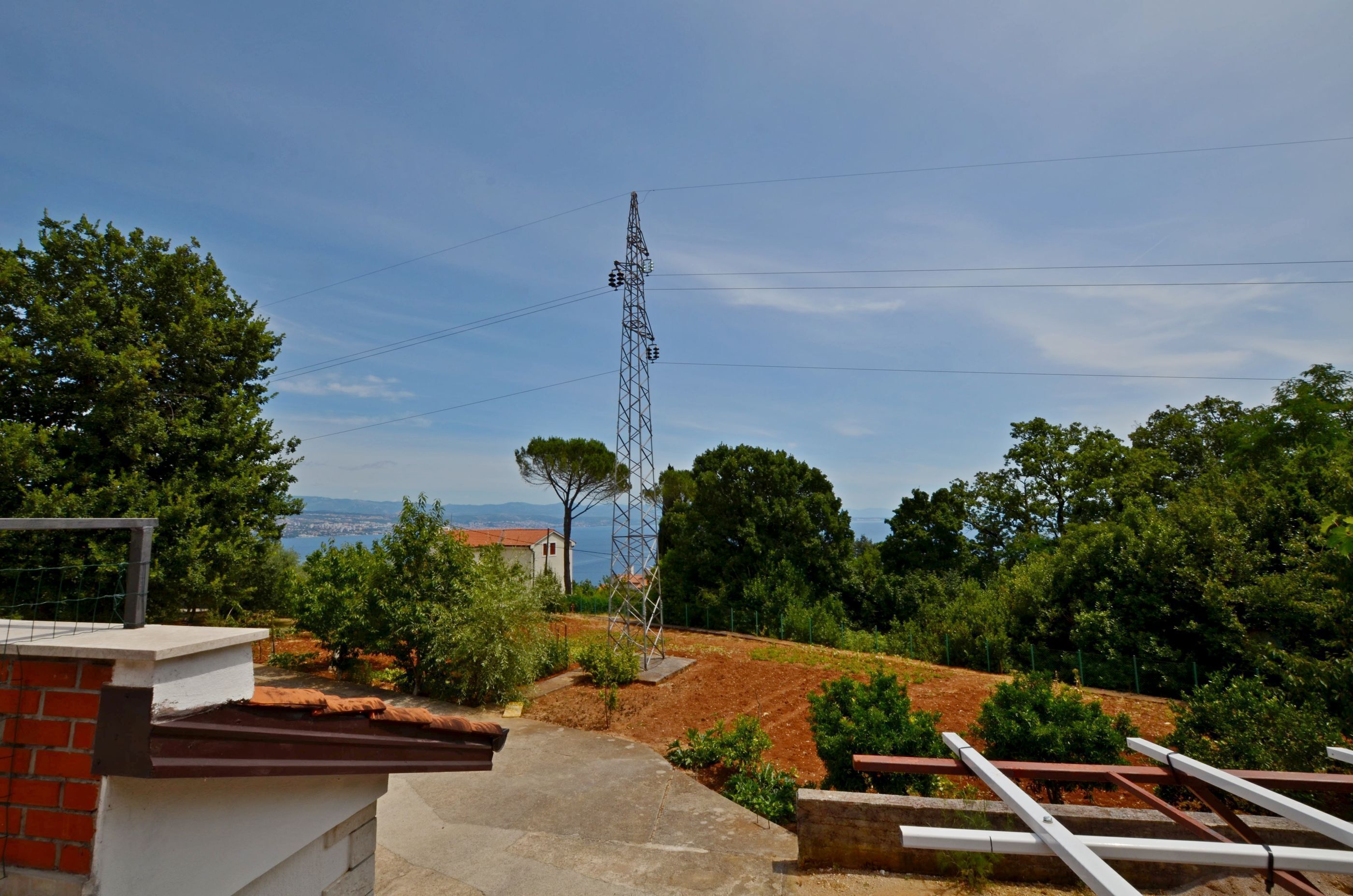 A residential area with a tall electrical tower, a paved pathway, and a view of distant buildings and trees.