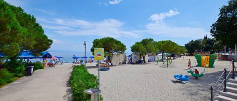 A beachside park with a sandy area, playground equipment, and a clear blue sky.
