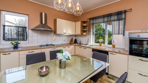 Eine moderne Küche mit einem Glastisch, Pendelleuchten und einem eingebauten Backofen.