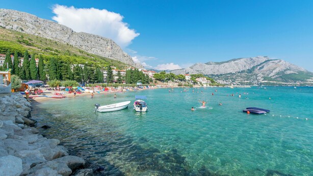 Eine Küstenlandschaft mit klarem türkisblauem Wasser, felsigem Ufer und einem gebirgigen Hintergrund.