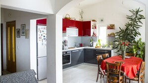 Eine kleine Küche mit roten Schränken, einem Esstisch mit Stühlen und einem Kühlschrank.